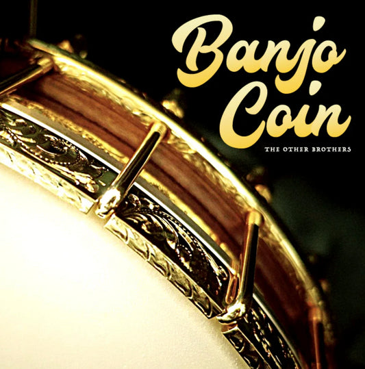 Close-up of a banjos rim and head with gold hardware. The words Banjo Coin appear in large, yellow script in the upper right, and The Other Brothers is written below in small, white text—highlighting magic tricks you can buy.