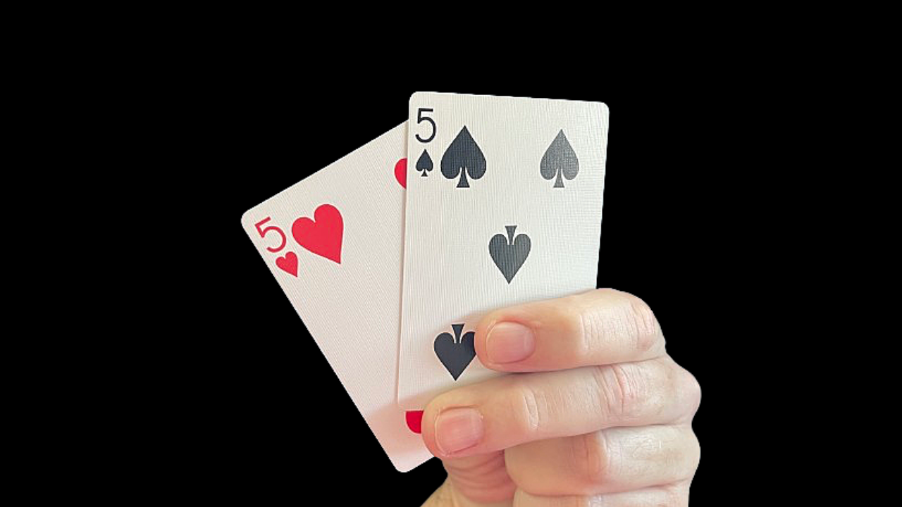 Hand holding two playing cards with face value of five of hearts and five of spades