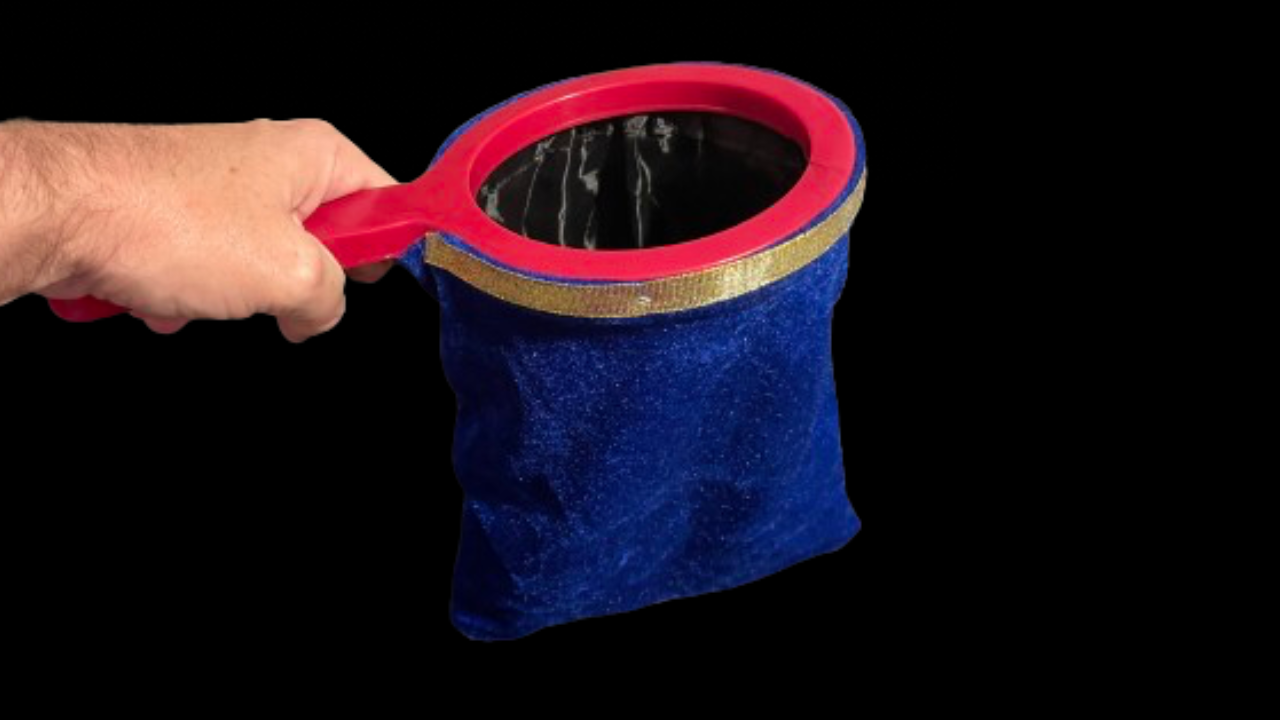 Hand holding blue velvet change bag with zipper and a red handle, used in a magic trick.