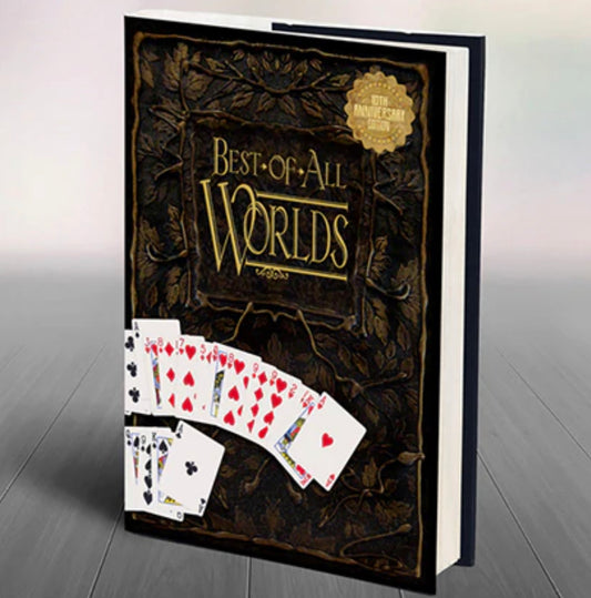 A large magic book for sale titled Best-of-All Worlds, with an ornate black and gold cover, stands upright on a table. Several playing cards are fanned out at the book’s base. A gold sticker marks the 10th anniversary edition.