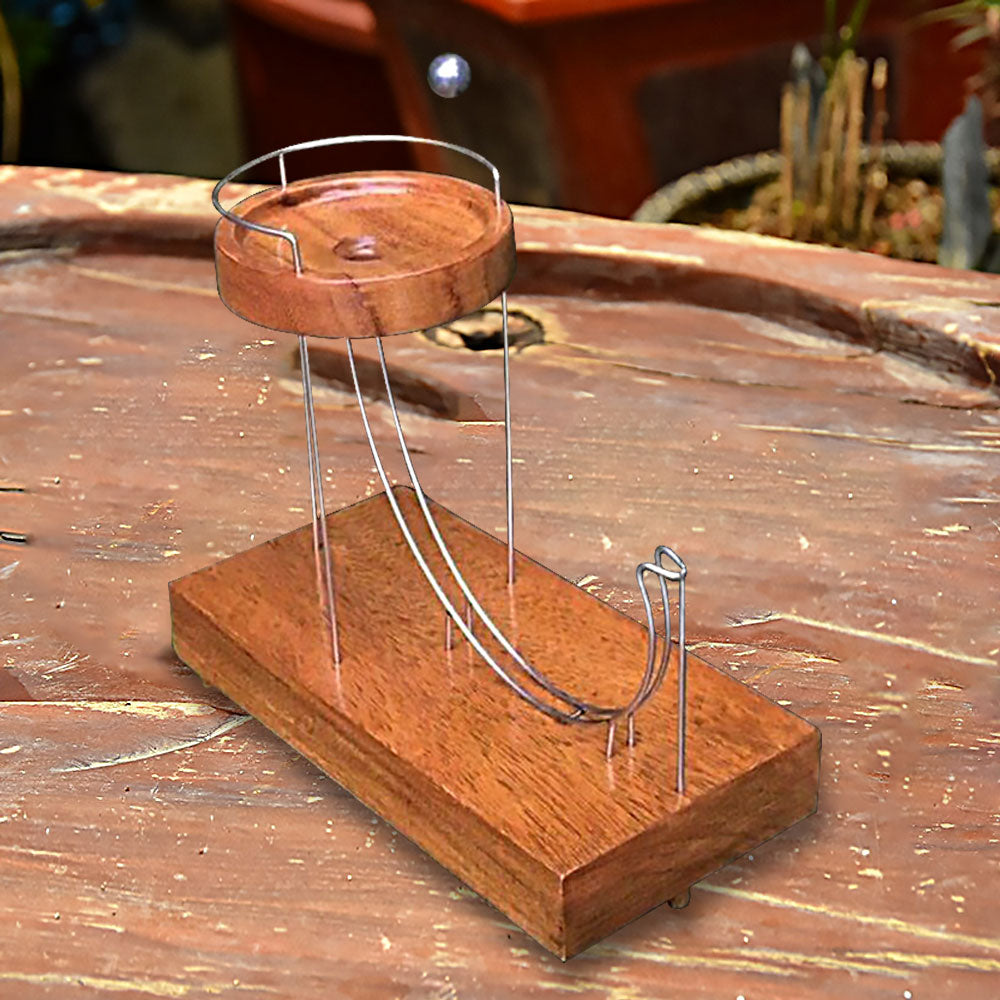 Wooden ball-launching toy with two metal ramps and a circular wooden platform on a wooden background.
