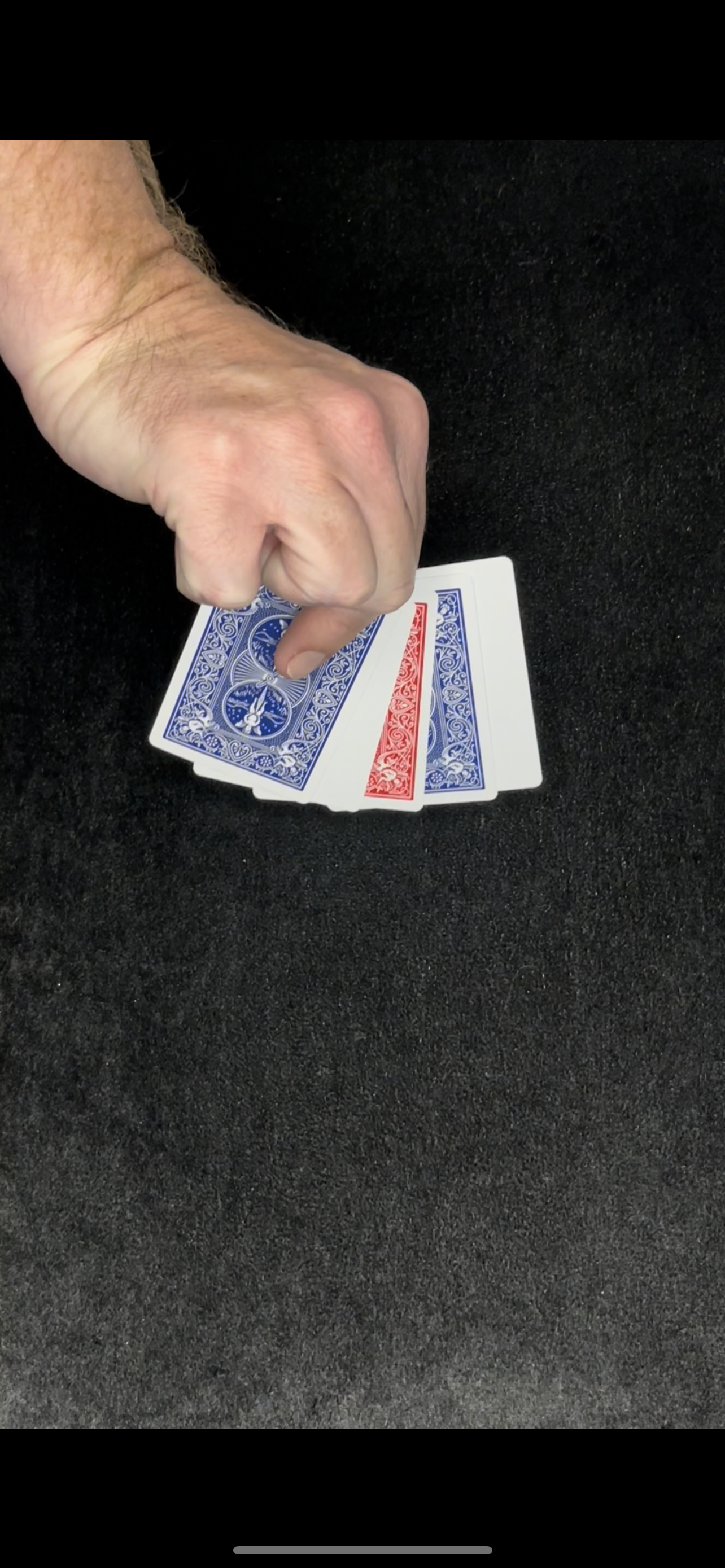Hand holding a fan of playing cards, blue and red backs visible, on a black surface.