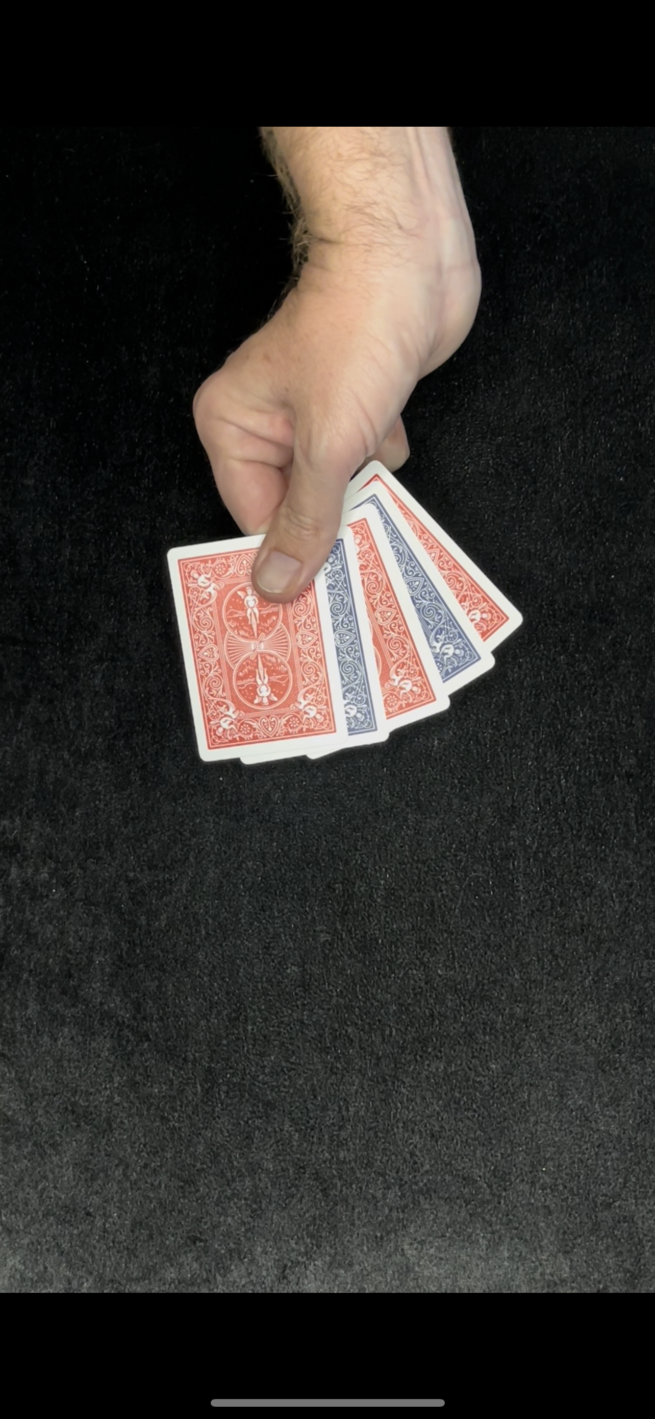 Hand holding a fan of playing cards, red and blue backs.