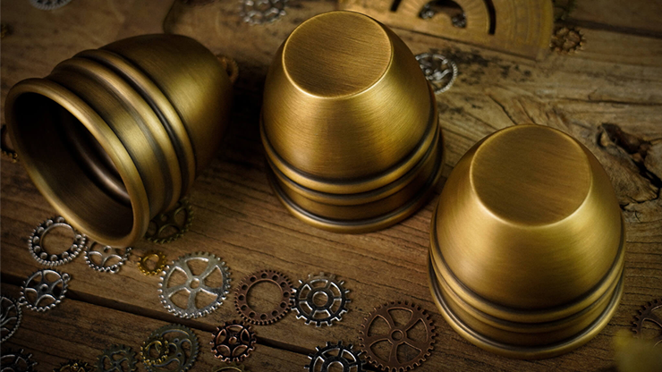 Three brass cups displayed with one on its side used in the magic cups and balls trick